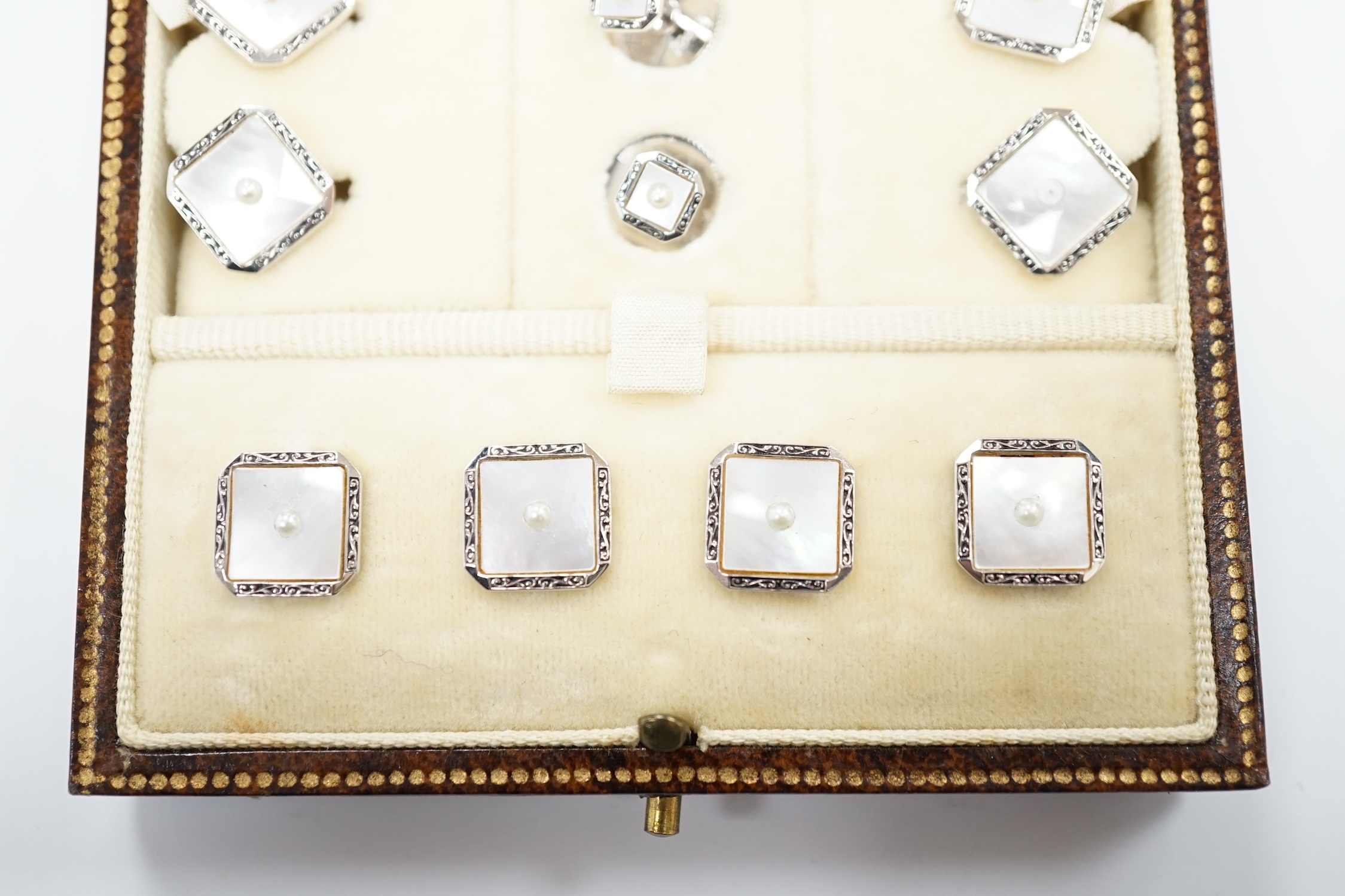 A 9ct white metal, mother of pearl and seed pearl set eight piece dress stud set, in fitted gilt tooled leather case.